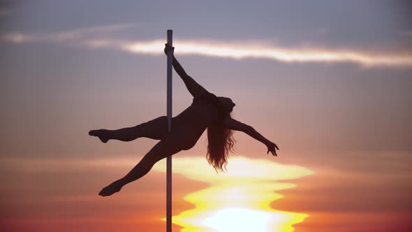 Young Woman Holding on the Top of Dancing Pole on Sunset