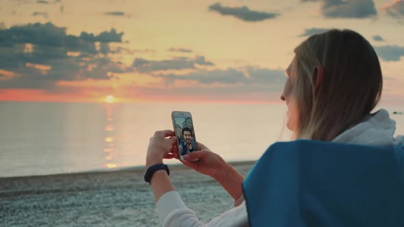 Young Woman Making Video Call to Her Friend with Smartphone on the Beach