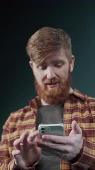 Redhead Guy in Modern Plaid Shirt Look Into the Screen of New Popular Mobile Phone