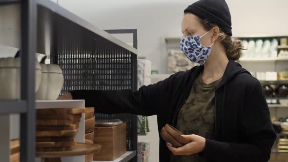 Young Woman Wearing Protective Face Mask Chooses Wooden Pottery in in Dinneware Department of Home