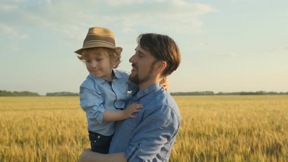 Happy father holding his little son on shoulders and walking at meadow on sunny summer day. 