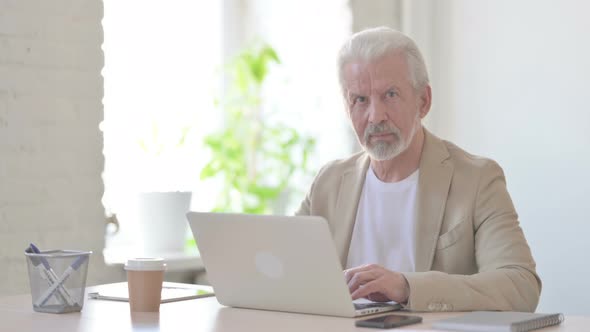 Old Man Looking at Camera While Using Laptop in Office