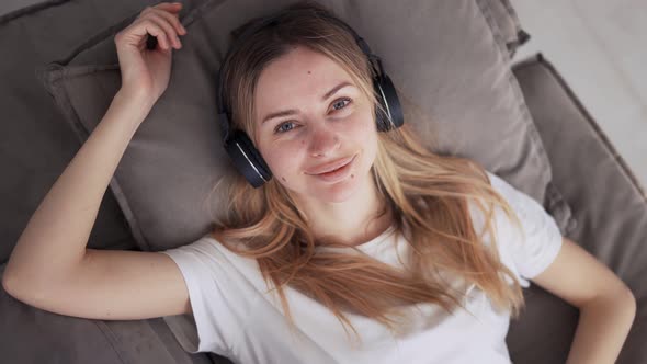 Woman Relaxing and Enjoying Music in Headphones on Couch