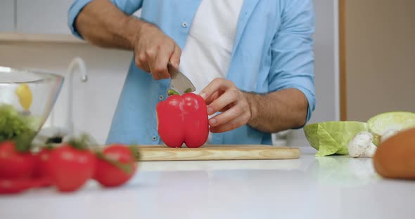 Man Cutting on Two Parts Red Pepper on Cutting Board while Preparing fresh Vegetable Salad