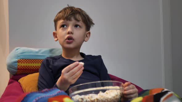 The Child Lies on the Couch and Eats Popcorn