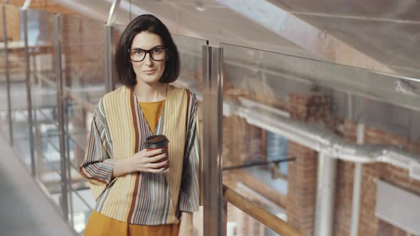 Positive Woman Holding Coffee Cup and Posing for Camera in Office