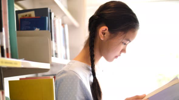 Asian teenager student reading a book in school library.