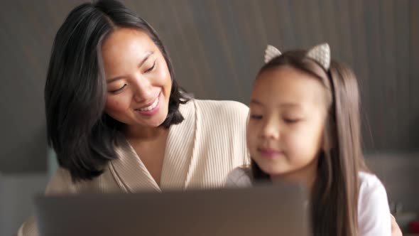 Positive Asian mom and daughter looking at laptop