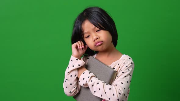Portrait of cute Asian schoolgirl child 7-8 years looking at camera standing and holding book on the alt