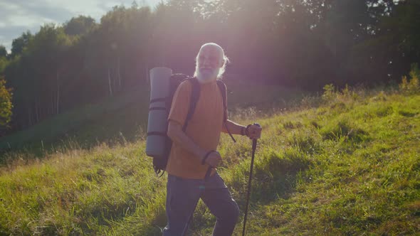 Happy Elderly Man with a Backpack and Nordic Walking Poles Walks Along