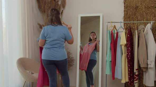 Plussize Woman Comparing Dresses Standing in Front of Mirror Indoors