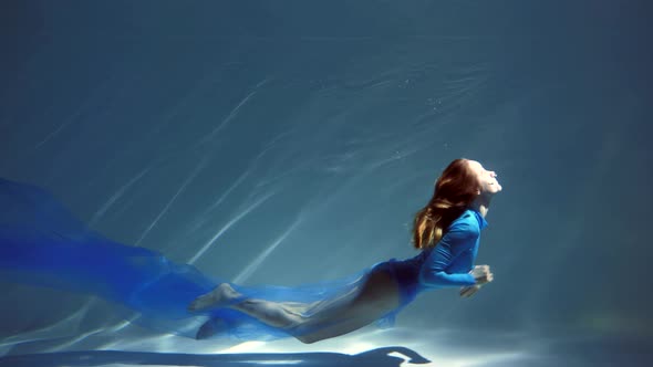 Attractive Young Woman Swims Beautifully Underwater in a Blue Dress Dress