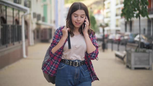 Front View of Charming Confident Caucasian Teenage Girl Talking on Phone Smiling Walking on City