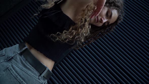 a Young Woman with Curly Hair Poses Against a Dark Gray Wall. the Camera Is Moving