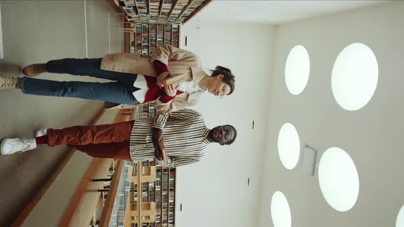 Multiethnic Man and Woman Walking in Library and Discussing Books