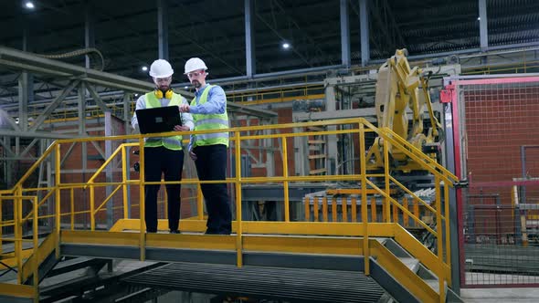 Two Male Specialists Talking Near Modern Industrial Equipment