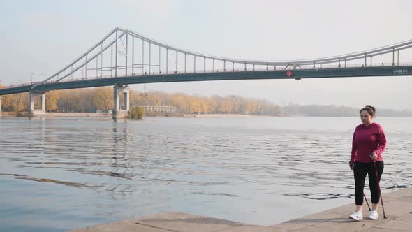 Business Woman Nordic walking training before work along city river with bridge and park