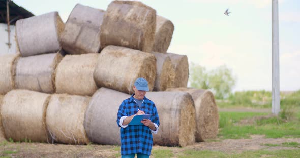 Farmer Gesturing While Writing on Clipboard Against Barn