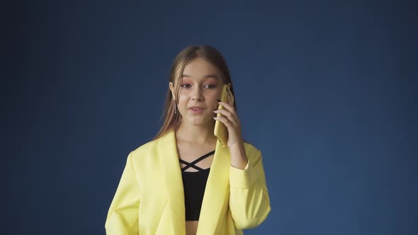 A Young Teenage Girl Talking on the Phone Against a Blue Background