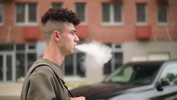 Stylish young man walks through the city and smokes an electronic cigarette