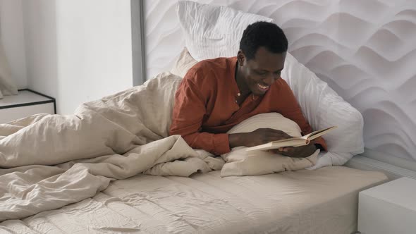 Happy AfricanAmerican Man in Pajama Reads Book Lying in Bed