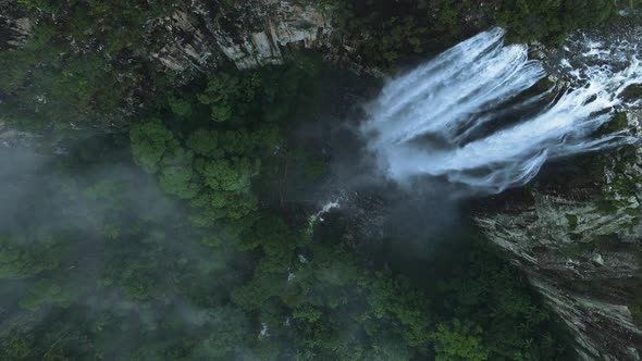 Lush tropical waterfall spilling down into a large crater covered rainforest mountain. Unique drone