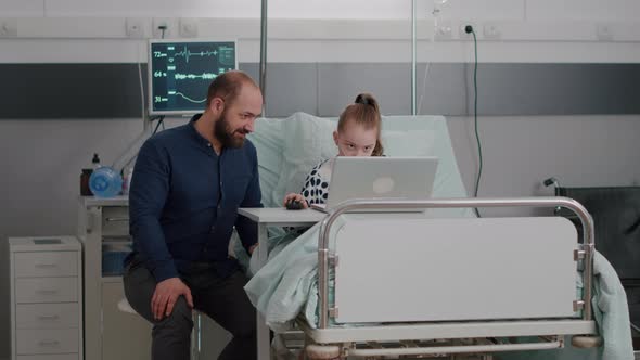 Father Sitting Beside Sick Daughter While Playing Cartoon Online Video Games Using Laptop Computer