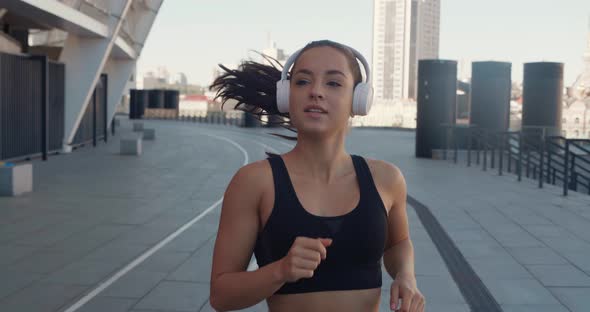 Front View of Athletic Young Woman in Headphones Jogging and Listening Music Outdoors in Slow Motion