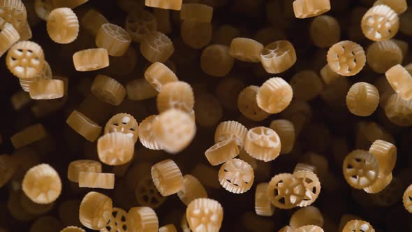 Raw wagon wheels pasta flies after being exploded against black background. Slow Motion.