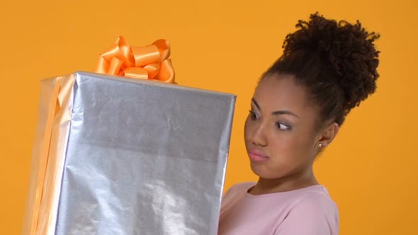 Pretty African Female Hardly Holding Big Present Box on Bright Background, Gift