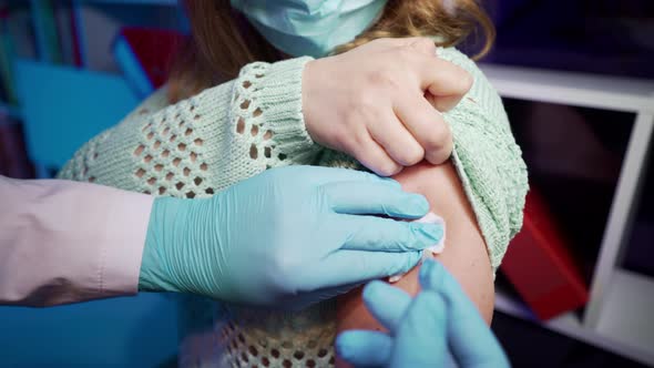 A doctor in protective gloves and a mask injects a coronavirus vaccine to a patient in a hospital.