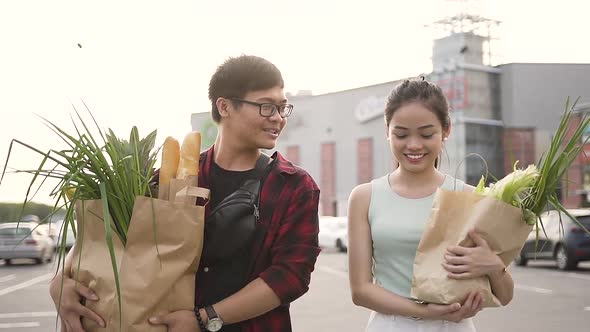 Cheerful Asian Man and Woman Holding Big Food Bags Near the Supermarket