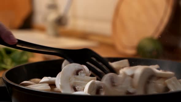 Close-up of Woman with Wooden Spatula Interferes with Chopped Champignon Mushrooms in Pan. Slow