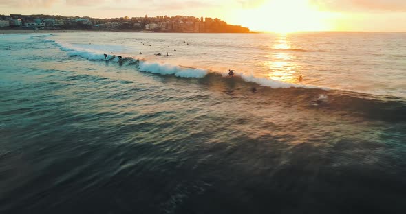 Tracking aerial shot of a surfer catching a wave at Bondi Beach during sunrise.