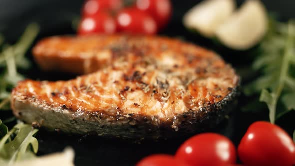 A Cooked Salmon Steak with the Addition of Aromatic Spices and Vegetables on a Black Serving Plate