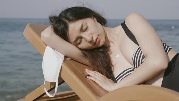Pretty Asian Woman Sleeping at Beach Deck Chair with Medical Mask Tired of Coronavirus Pandemic