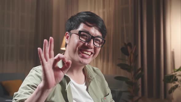 Asian Man Sitting In A Wheelchair Smiling And Showing Ok Sign In Living Room