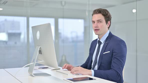 Cheerful Young Businessman Pointing Finger at Camera in Office 