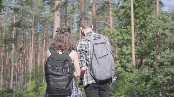 Portrait of Guy and Young Girlfriend Walking in the Forest. Pair of Travelers with Backpacks