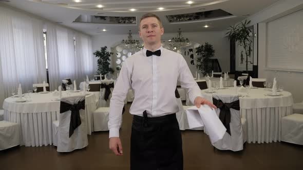Portrait of a Waiter in a Restaurant Against the Background of Served Tables