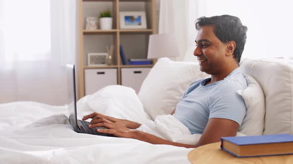 Happy Indian Man with Laptop in Bed at Home