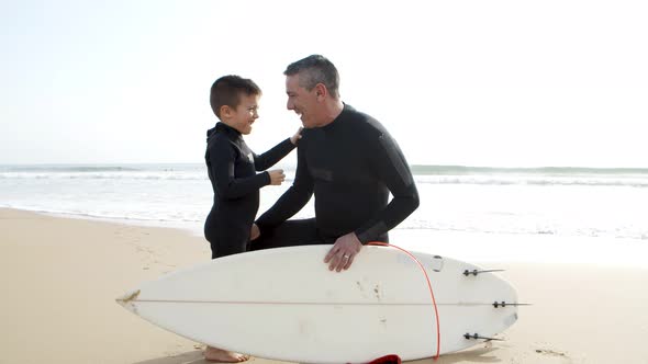 Father and Son in Wetsuits Talking on Beach