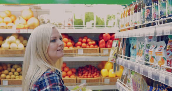 Attractive Woman is Walking Near the Supermarket Shelf and Selects the Products