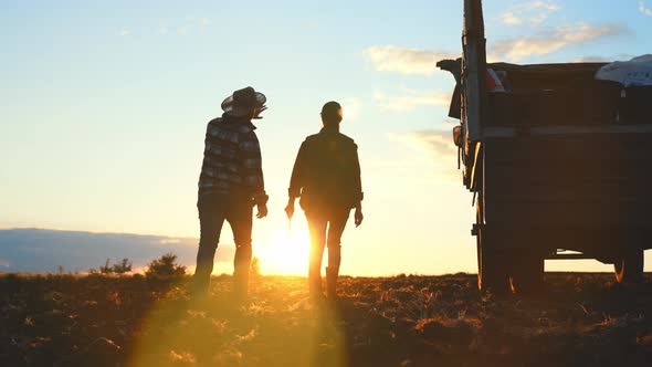 Silhouette Farmer Woman and Man Engineer with Digital Tablet Walking in Field in Rays of Sunset on