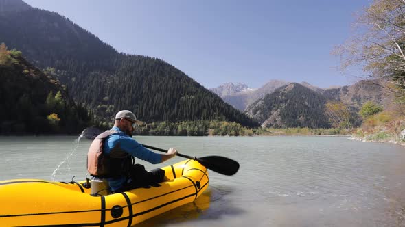 Man is Paddling on Raft Boat in the Mountain Lake