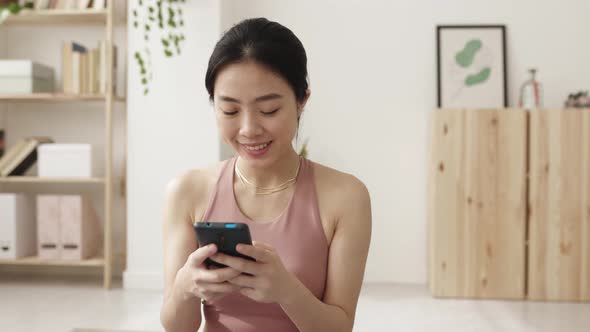 Young Asian Woman Using Mobile Phone After Workout Exercise Routine at Home