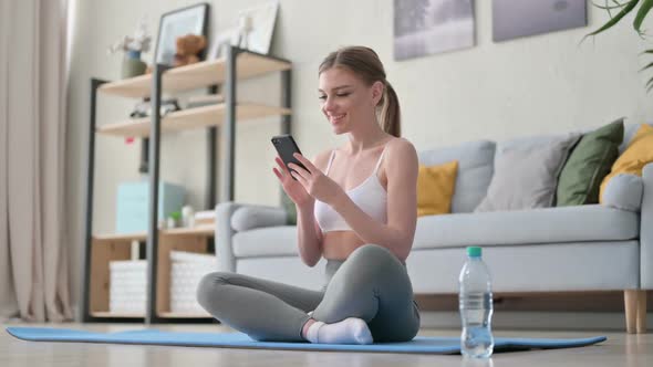 Young Woman Using Smartphone on Yoga Mat at Home