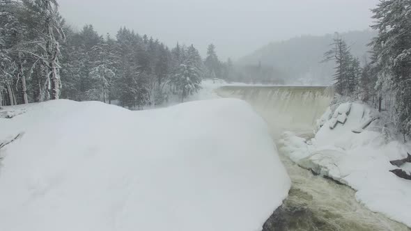 Dreamy aerial flight over cascading river of water flowing thru dense snow