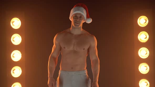 Portrait of Muscular Man Wearing Christmas Santa Hat Standing on Smoky Background