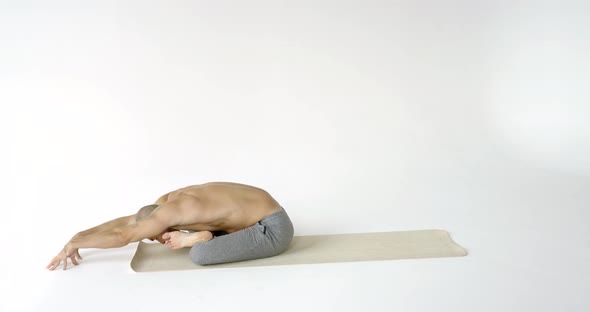 A Flexible and Plastic Male Yogi with a Beard Does Yoga on a Rug in a White Studio